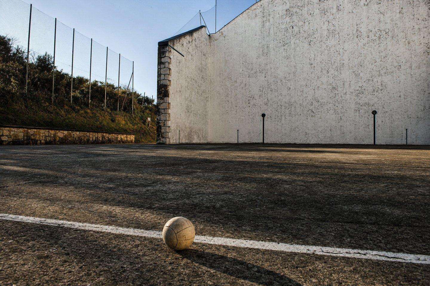 A traditional Basque handball court with a player mid-serve against a stone wall