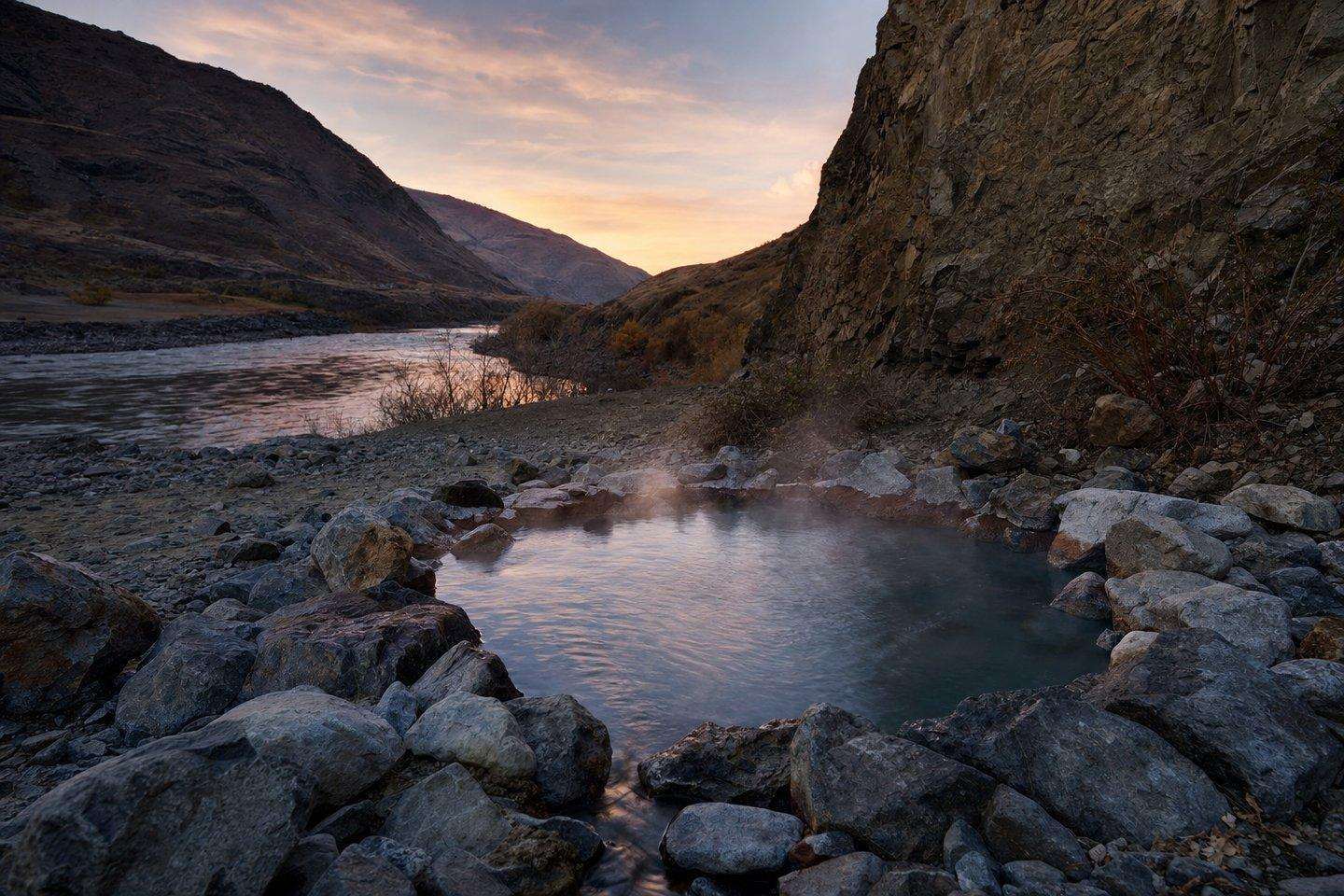 Steam rising from a natural hot spring pool at dusk in a river canyon
