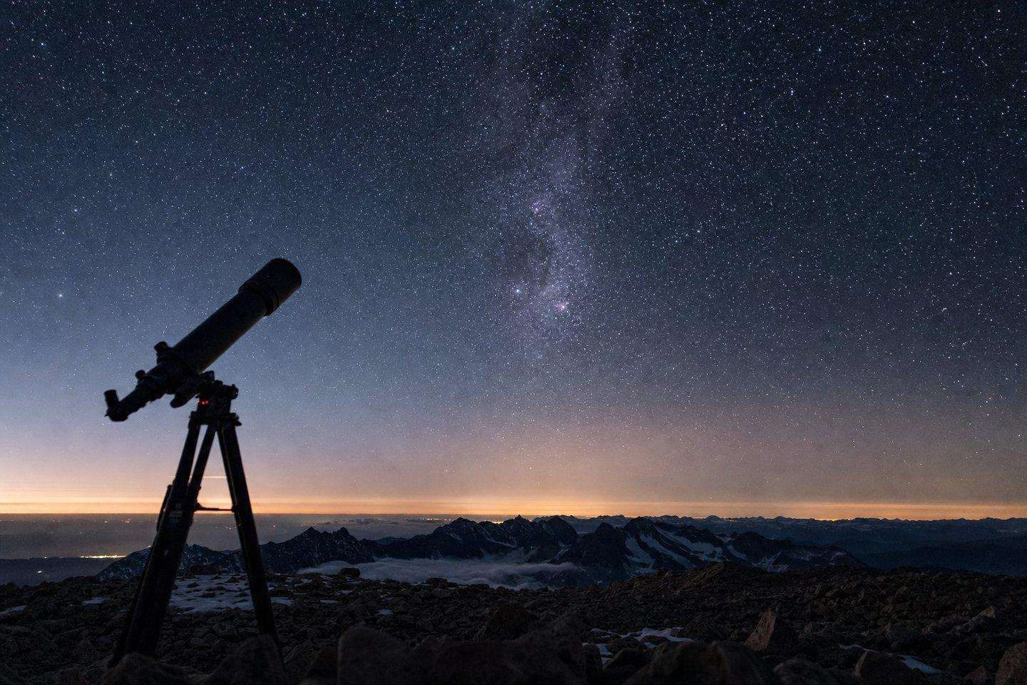 A telescope silhouetted against a star-filled sky at a high-elevation mountain overlook