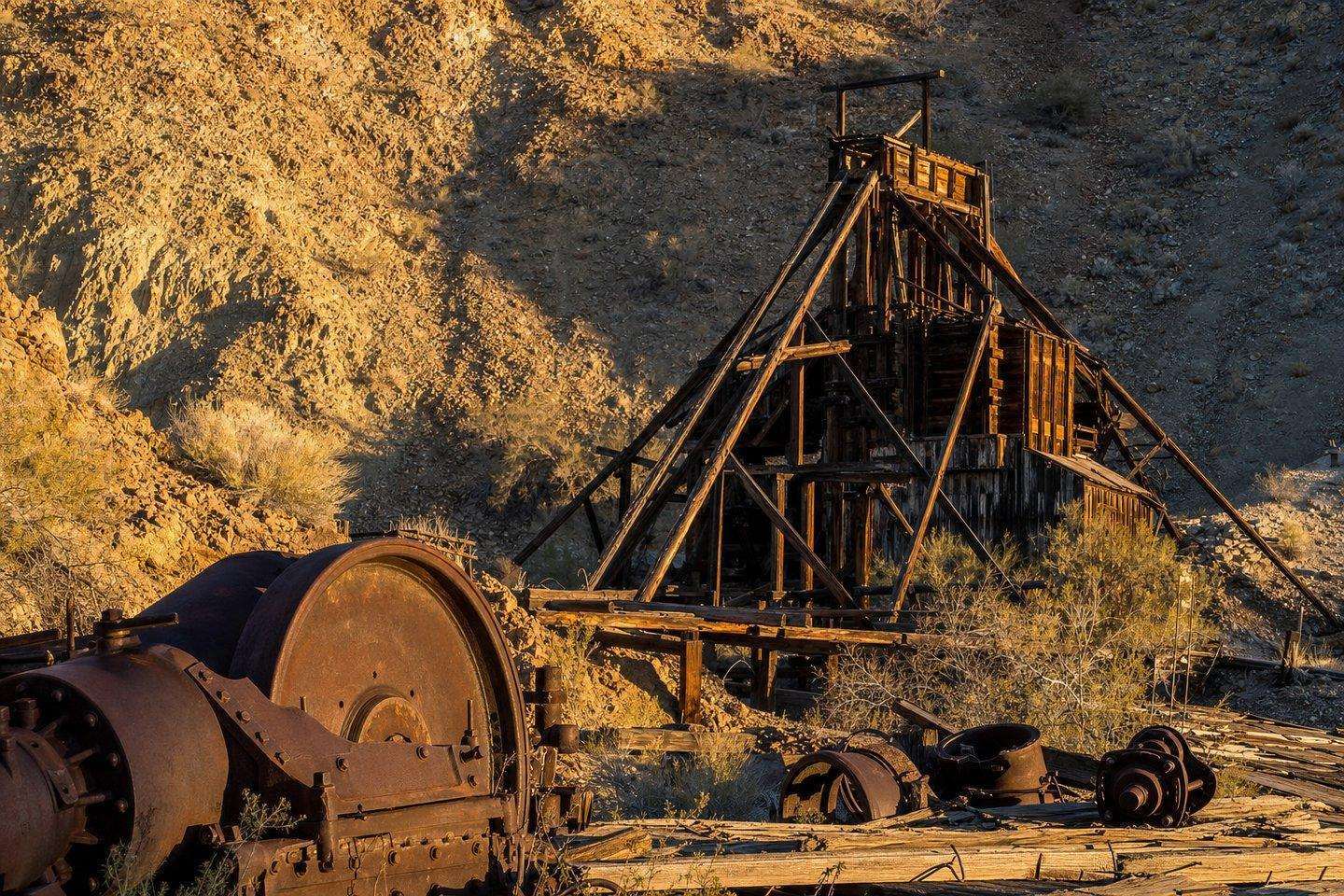 Rusted historic mining equipment and weathered wooden headframes on a desert hillside